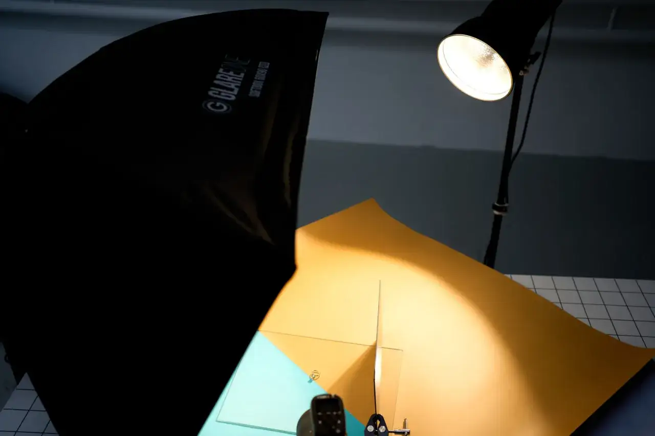 Studio flat lay: softbox GlareOne, lamp, and colorful paper backgrounds ready for a photoshoot.