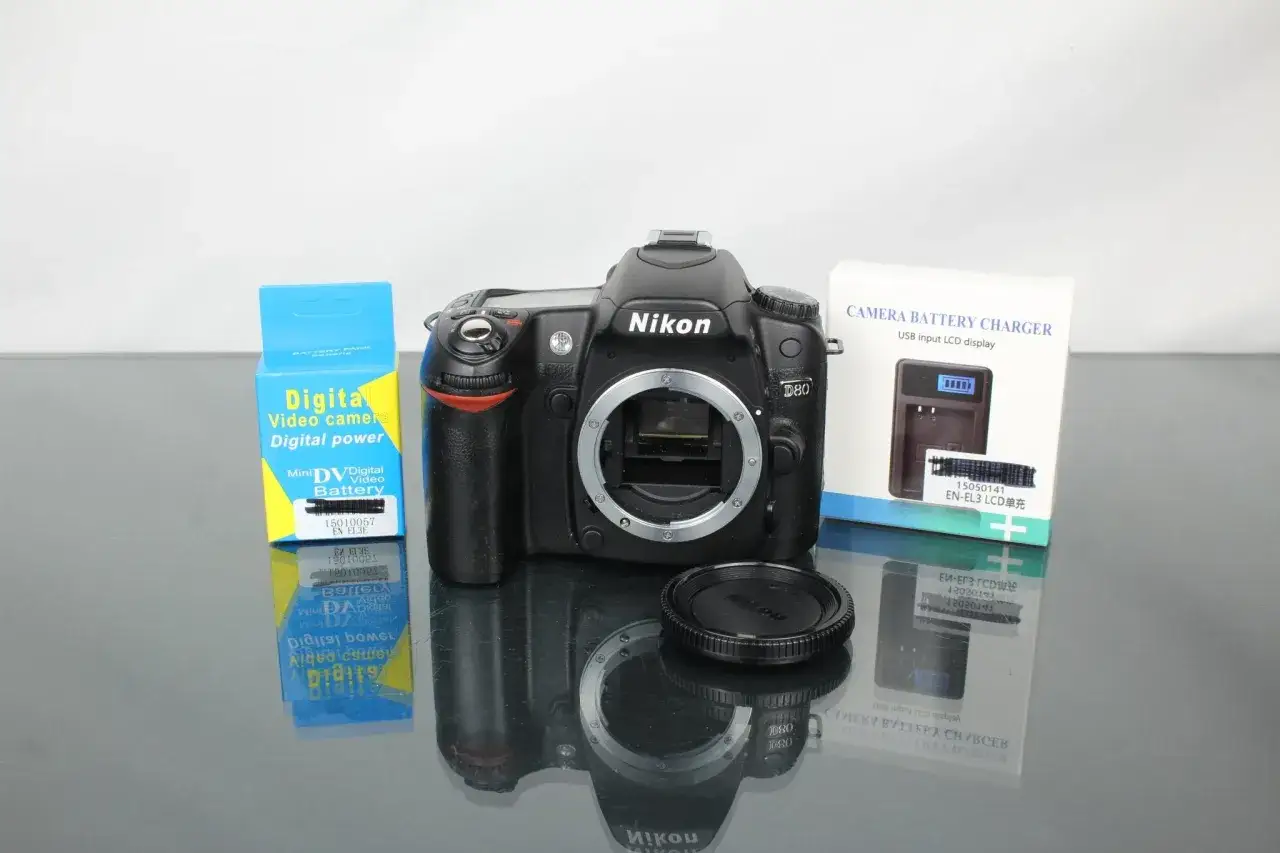 Nikon D80 z akcesoriami: ładowarka, bateria i dekielek obiektywu.