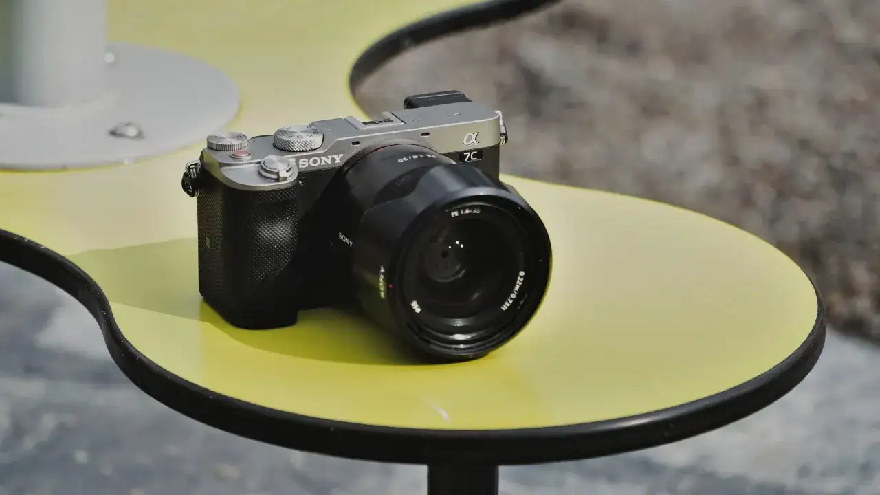 Srebrno-czarny aparat Sony a7c z obiektywem na żółtym stoliku.