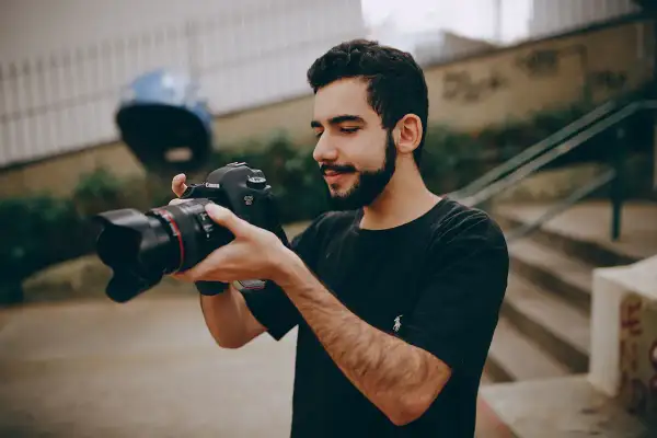 Młody mężczyzna z brodą trzyma w dłoniach swój pierwszy aparat Canon EOS 6D, gotowy do uchwycenia niezwykłych chwil.