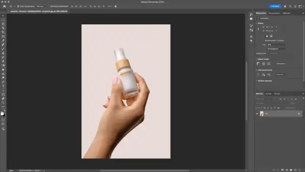 Dłoń trzymająca buteleczkę kosmetyku na jasnym tle. Program Photoshop pokazuje narzędzia, jak usunąć tło ze zdjęcia, aby wyizolować produkt.