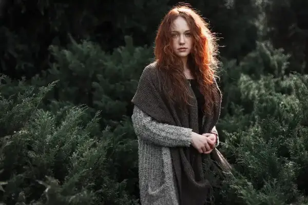 Ruda dziewczyna w otoczeniu zieleni. Minimalizm w fotografii podkreśla jej naturalne piękno i spokój.