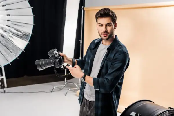 Młody fotograf z aparatem w studio. Chcesz wiedzieć, jak napisać opinie dla fotografa? Oto wskazówki!