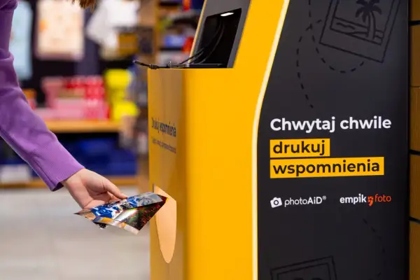 Ręka wkłada zdjęcia do automatu, by wydrukować wspomnienia w Empiku.