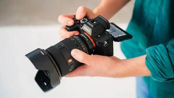 Dłonie trzymają aparat Sony a7r5 z obiektywem.