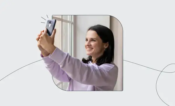 Uśmiechnięta dziewczyna robi selfie telefonem, jakby korzystała z automatu do robienia zdjęć do dowodu.