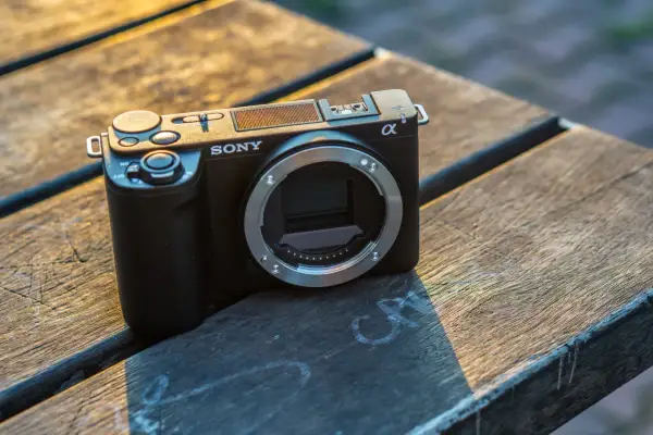Czarny aparat Sony Alpha ZV-E10 bez obiektywu leży na drewnianym stole.