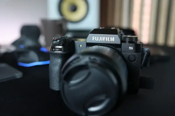 Czarny aparat Fujifilm xh2s z obiektywem i osłoną obiektywu na czarnym blacie.