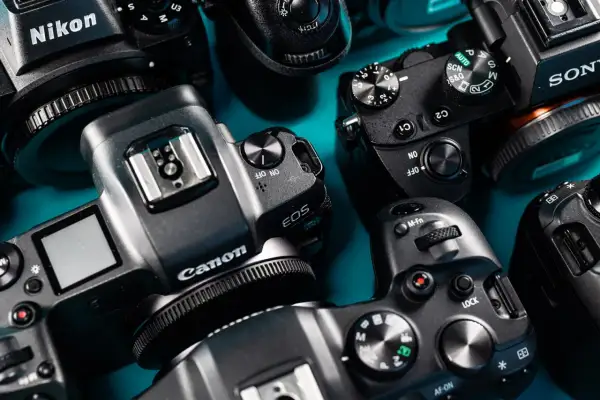 Zbliżenie na kilka aparatów fotograficznych marek Canon, Nikon i Sony ułożonych na niebieskim tle.